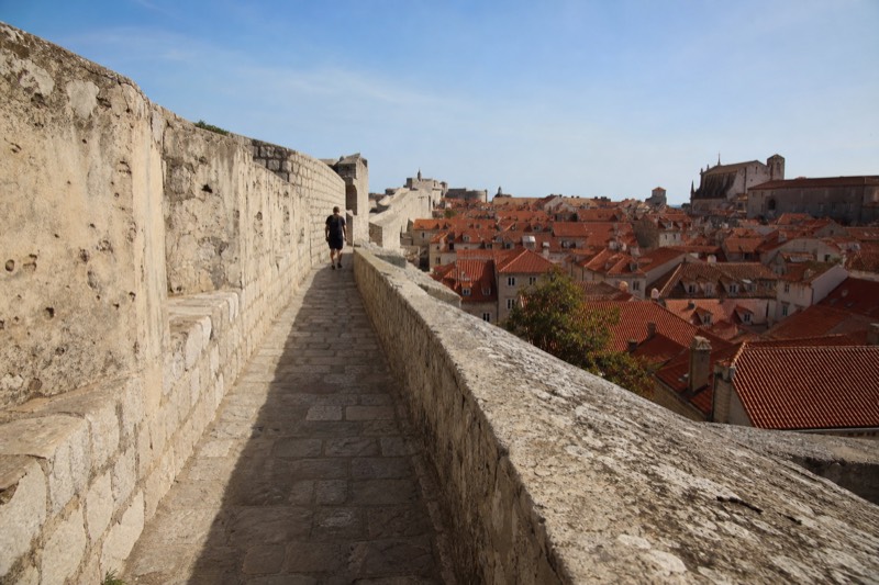 Looking down the sweep of Dubrovnik's fortress wall walk, weathered limestone parapets and patched shrapnel scars in the stone catch clear autumn morning light