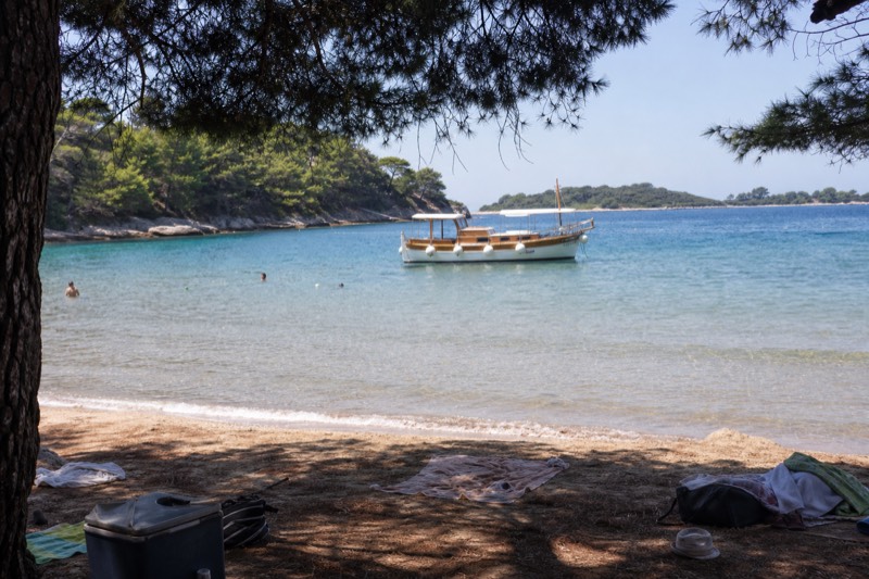 Morning at Šunj bay on Lopud in Croatia's Elaphiti Islands, shallow sandy water lapping pale sand, a wooden day-trip boat anchored offshore