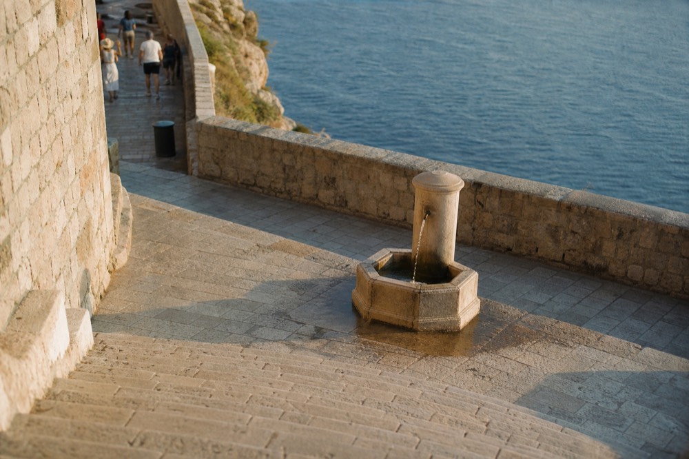 A public drinking fountain with a steady stream of water on a limestone square