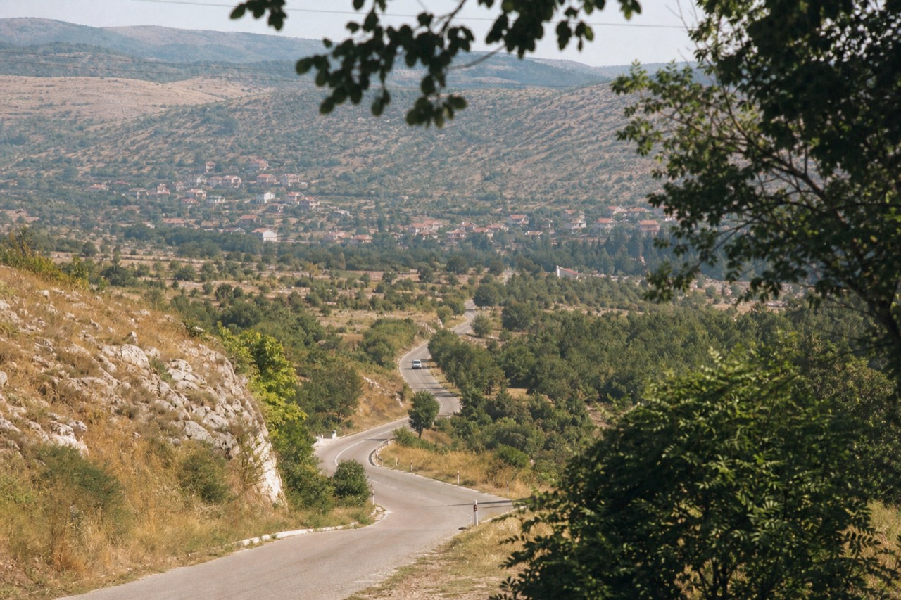 A country road winding through dry hills toward a small town in the Herzegovina interior