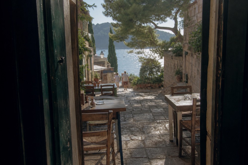 Cafe tables and rush-seated chairs set out on a narrow stone street in the afternoon