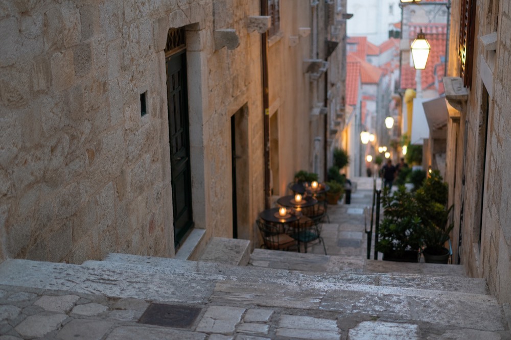 Lanterns glowing above a narrow stone street with outdoor tables in the evening