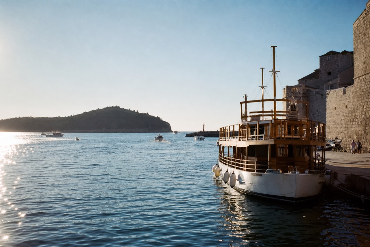 A wooden passenger boat moored in the Old City Harbour of Dubrovnik with Lokrum Island visible across the water