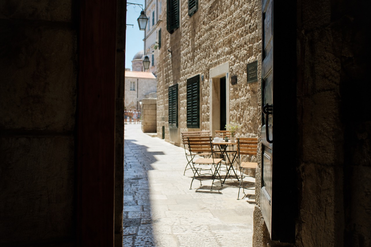 A stone street in Dubrovnik Old Town with café tables and shutters along the walls