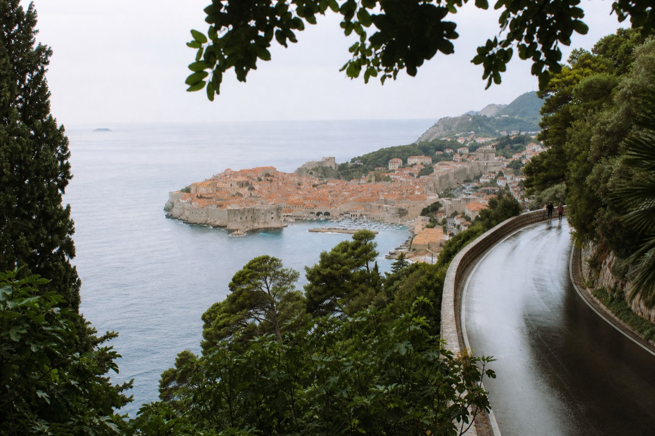 A coastal road winding along the Adriatic above a walled town with terracotta roofs