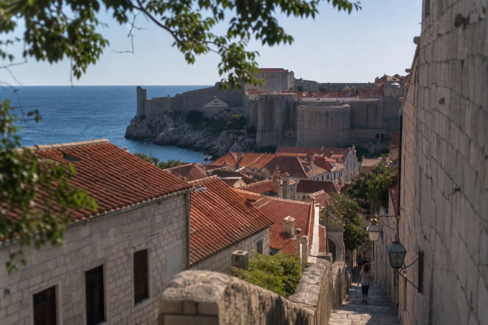 Stone city walls of Dubrovnik rising above red rooftops and the Adriatic sea