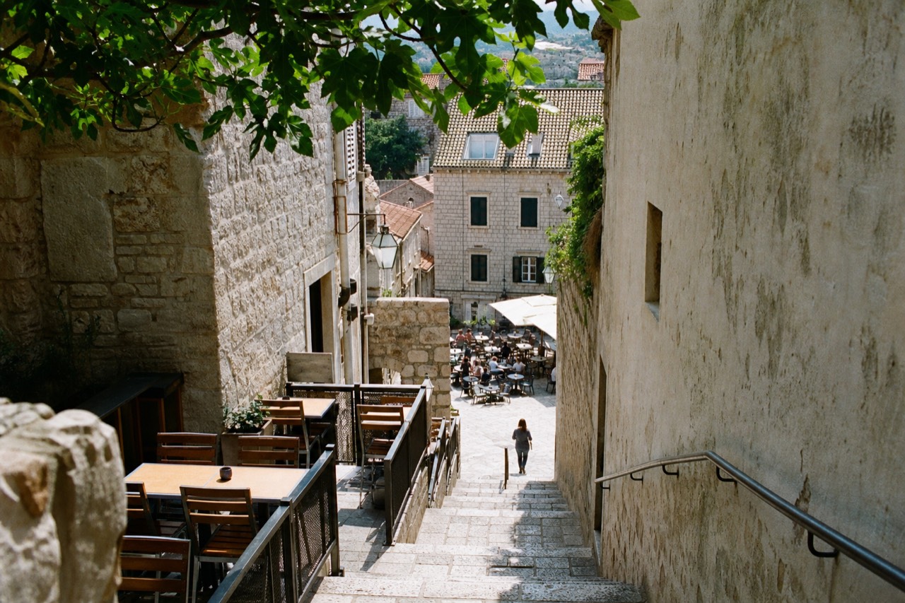 Sunlit limestone street in Dubrovnik Old Town with cafe tables and stone staircases