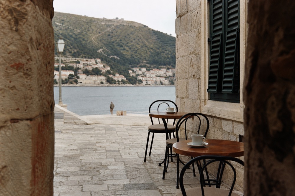 Cafe tables with coffee cups set out on a stone street beside a shuttered window