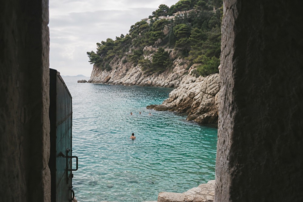 Swimmers in clear turquoise water beside rocky cliffs near Dubrovnik