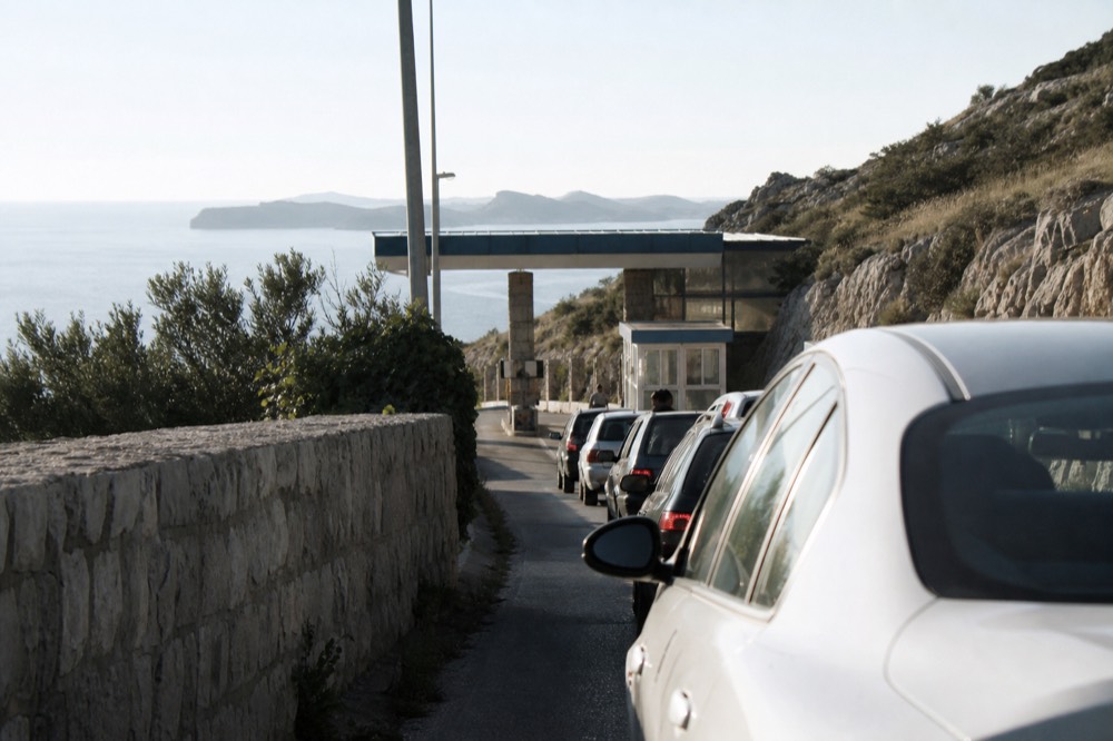 Cars queuing at a small border control booth between two countries on a sunny day