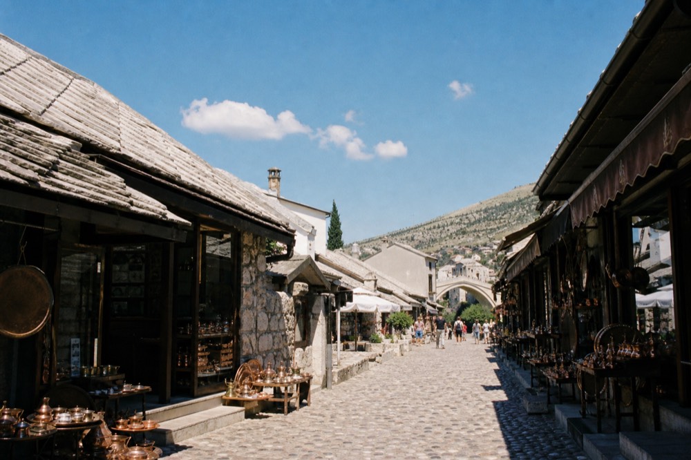Cobblestone bazaar street in Mostar lined with copper shops leading toward the old bridge