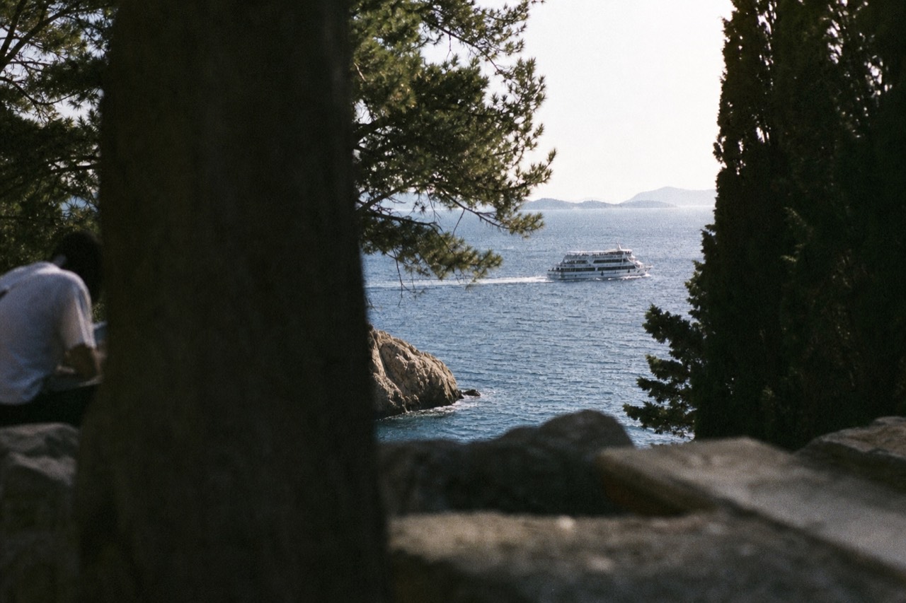 A passenger ferry cruising along a rocky Adriatic coastline with island silhouettes on the horizon
