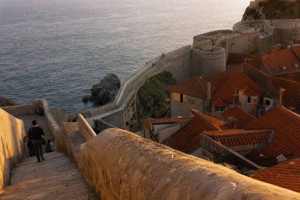 The stone fortifications of Dubrovnik's city walls curving above red rooftops toward the Adriatic Sea