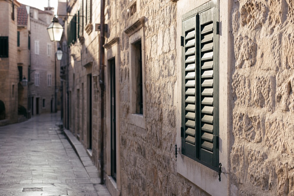 Empty limestone street inside Dubrovnik Old Town in soft winter light with shutters closed