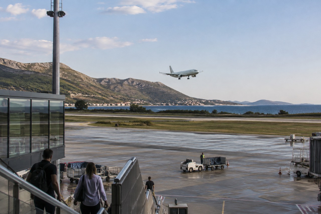 A plane descending over a coastal Croatian airport with dry hills behind the runway