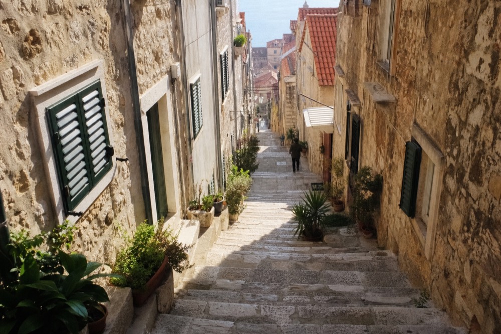 Narrow limestone street in an old Dalmatian town with shutters and potted plants