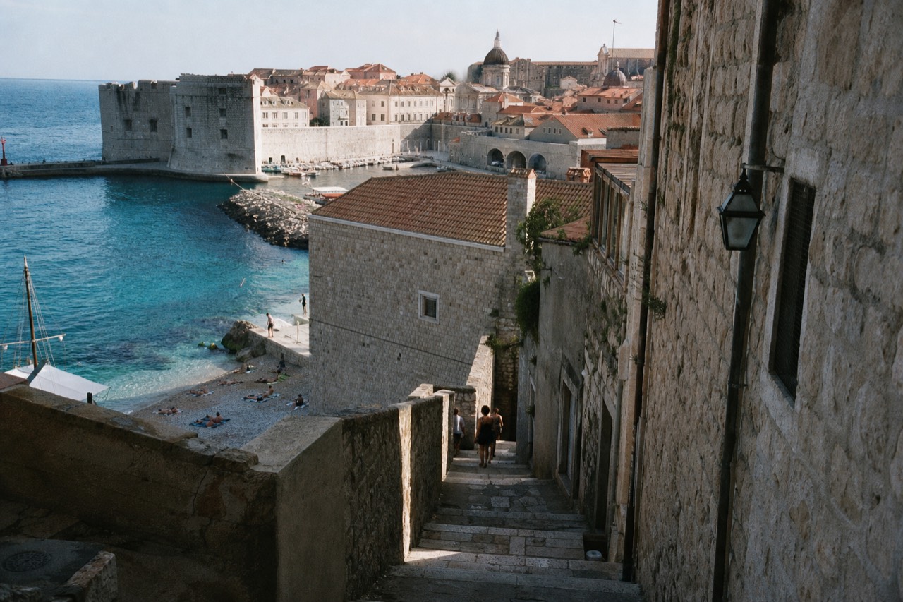 A pebble beach with clear turquoise water below a walled Adriatic town