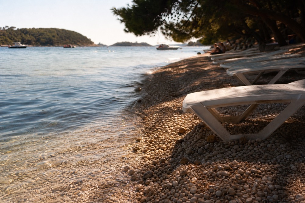 Pebble beach with clear shallow water and sun loungers under pine trees