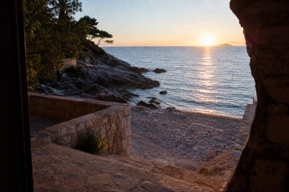 Rocky shoreline at sunset with the sun low over open sea and pine silhouettes