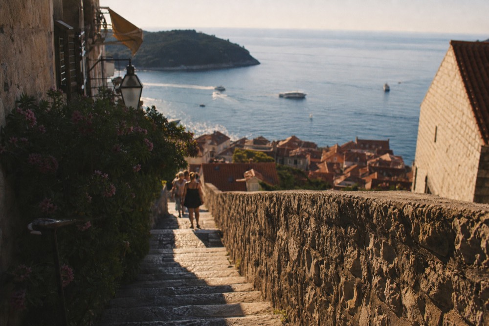 Stepped lane in Ploče with stone walls, bougainvillea and a view over red rooftops to the sea