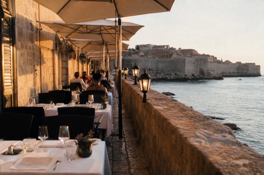 Hotel terrace with white tablecloths overlooking the sea and Dubrovnik walls in the distance