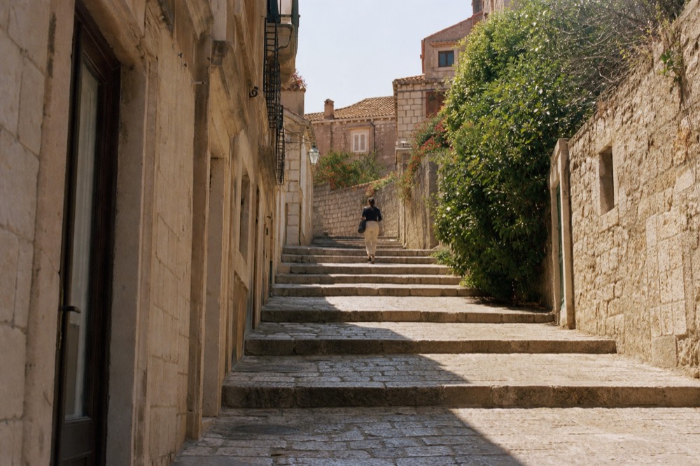 Sunlit limestone street in Dubrovnik with stone steps leading uphill between old buildings