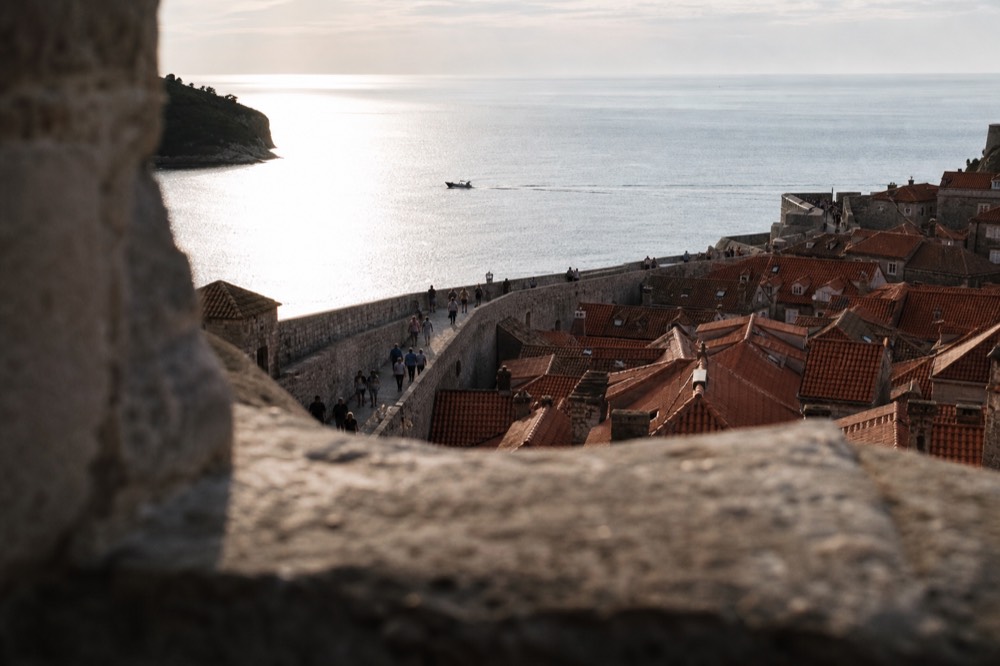 Walkers on the stone ramparts of Dubrovnik city walls above red rooftops