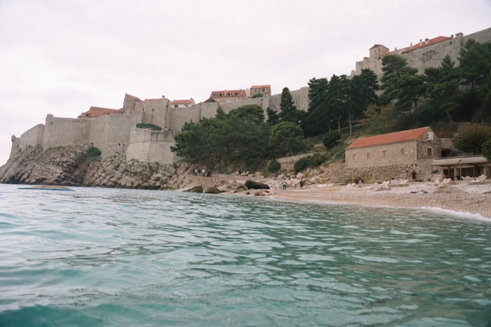 Pebble beach with clear turquoise water below Dubrovnik's walls