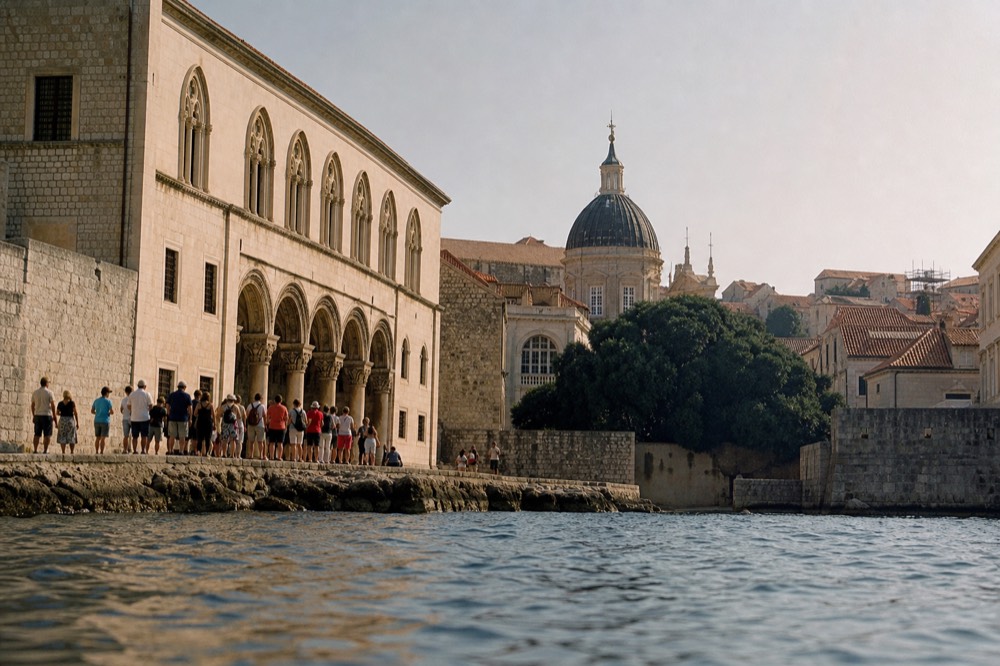 A group of visitors listening to a guide in front of the Rector's Palace, with the Cathedral in the background