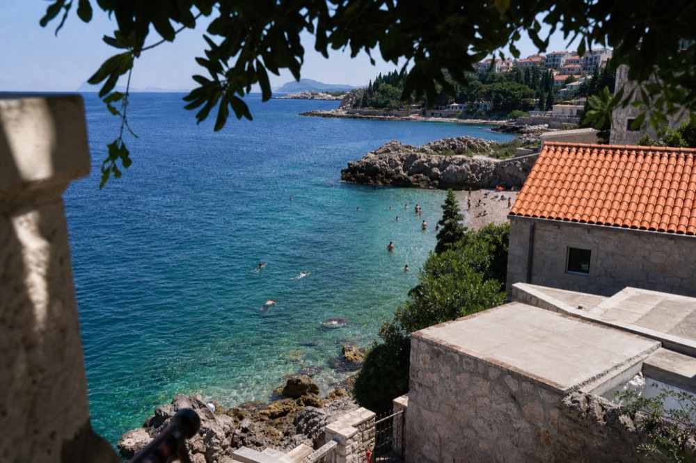 Swimmers in clear green-blue water a short distance from a pebble shore
