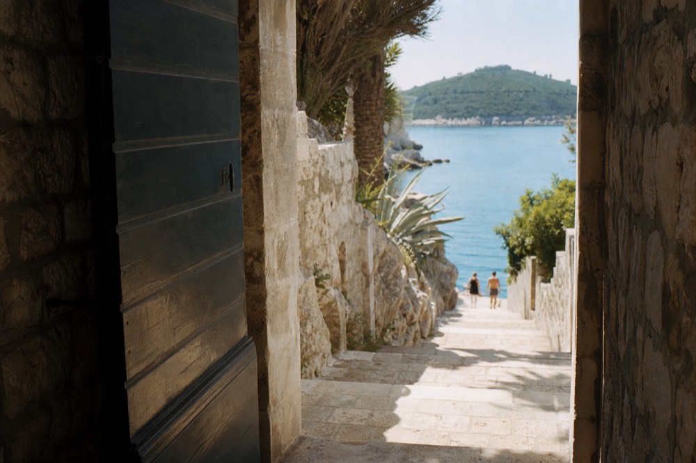 A stone gate opening onto a coastal path with sea and a green island beyond
