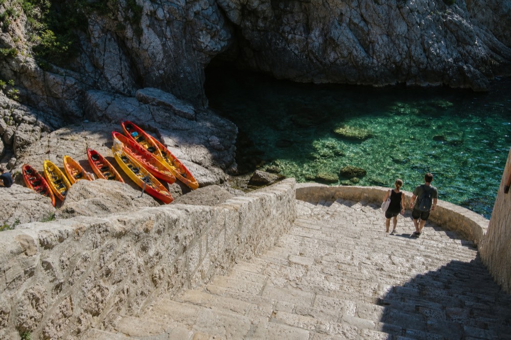 Kayaks pulled onto rocks beside a cave entrance and clear green water