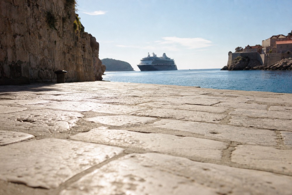 A cruise ship anchored off the Dubrovnik Old Town coastline in late afternoon light