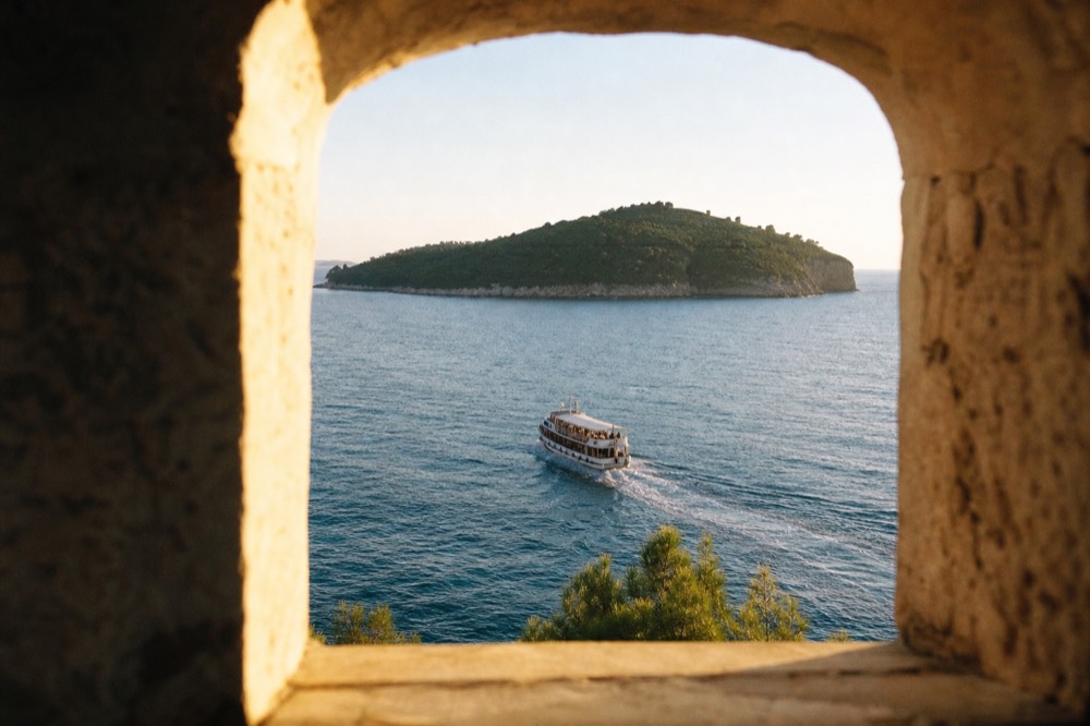 A small passenger boat crossing clear water toward a green island