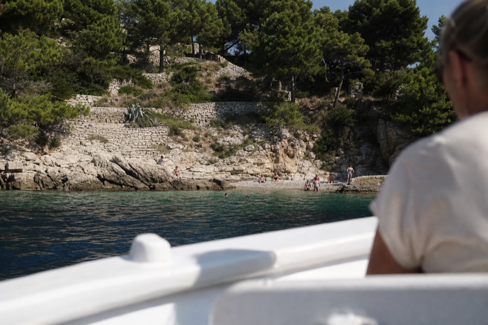 Passengers on a boat deck passing a rocky island coastline