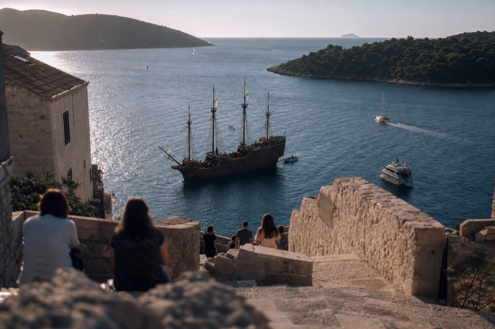 A wooden sailing ship anchored in a calm bay between green islands