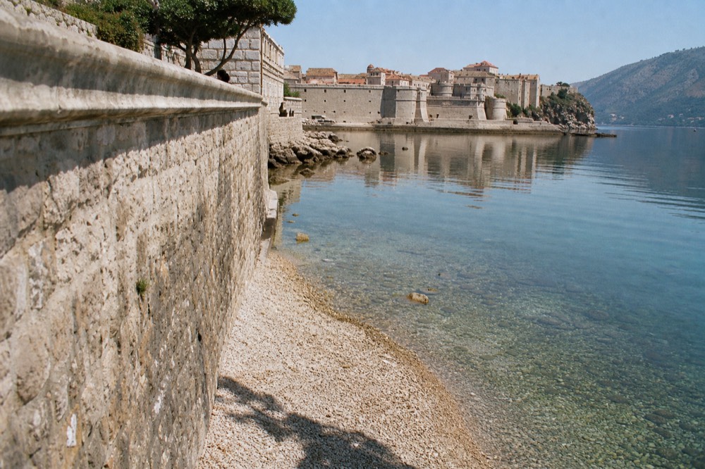 A walled medieval town reflected in still water at the head of a mountain bay