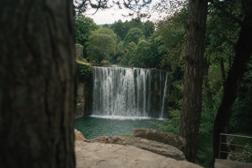 A wide waterfall spilling over a curved cliff face into a swimming hole
