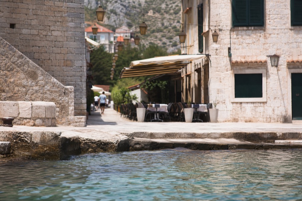 Outdoor cafe tables on a narrow stone street with hanging lanterns above