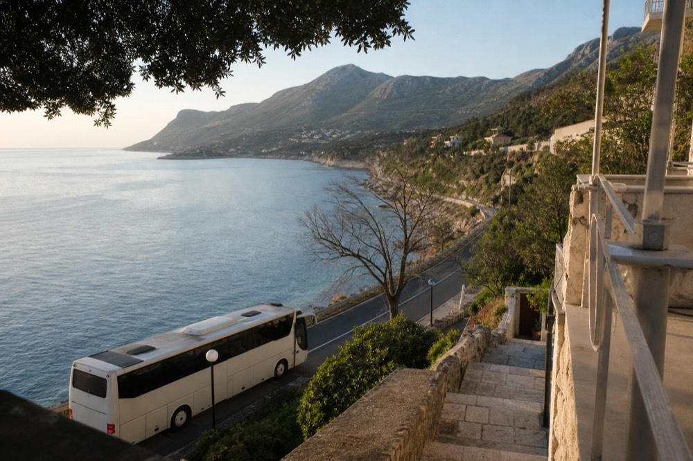 A coach parked on a coastal road with steep mountains rising across a bay