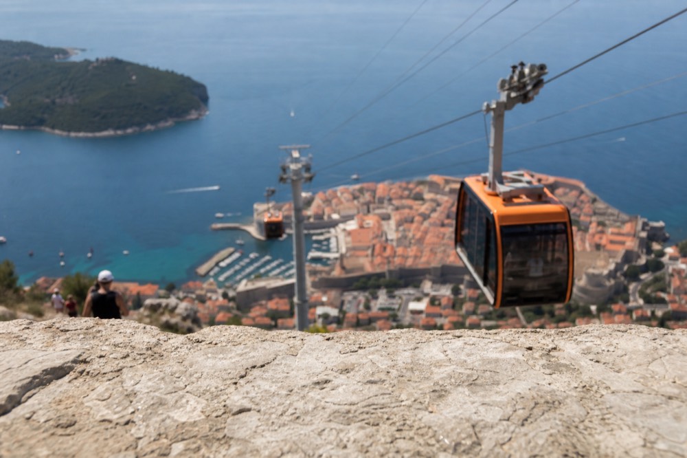 Cable car cabins travelling on a cable above a walled city and the sea