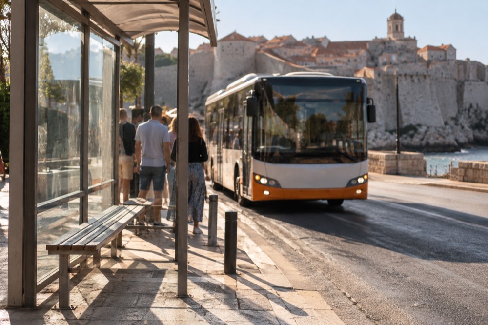 A shelter and kerb at a sunny bus stop near Dubrovnik Old Town, a bus pulling in behind