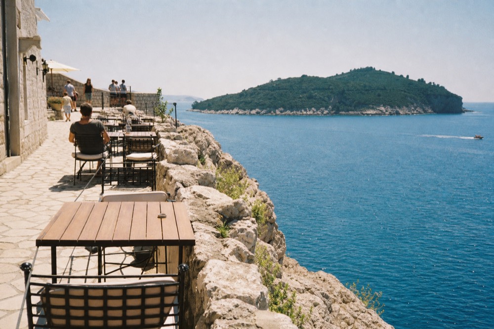 A rocky terrace with simple tables overlooking the blue Adriatic Sea and a green island