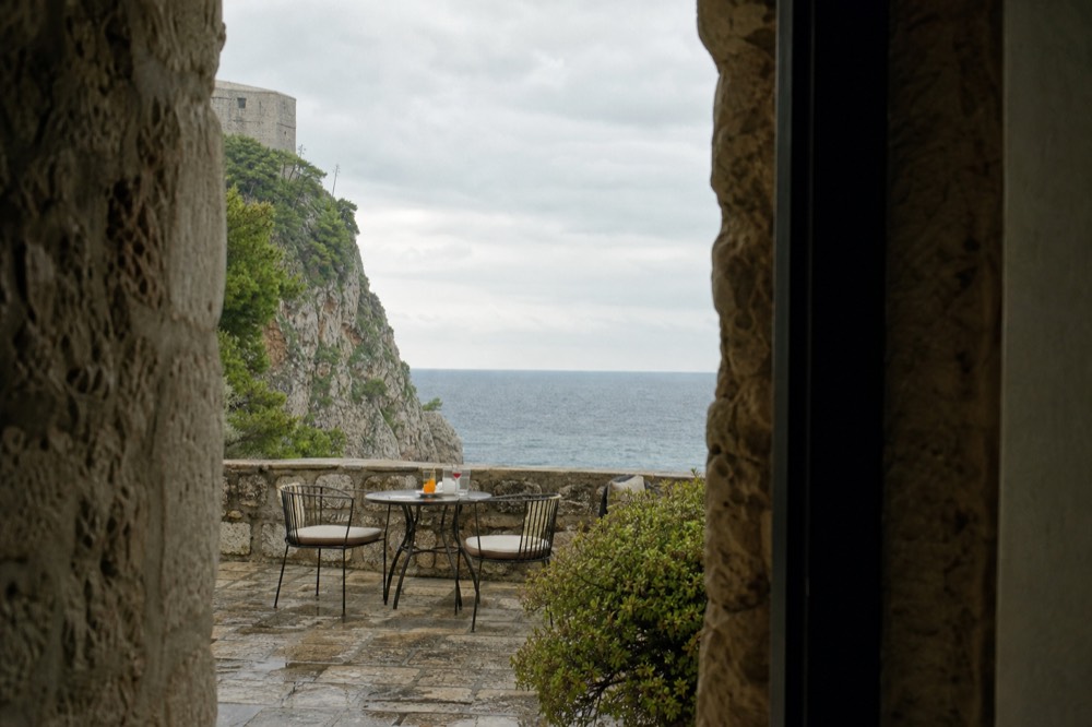 A simple cliffside terrace with drinks on a table and open sea beyond