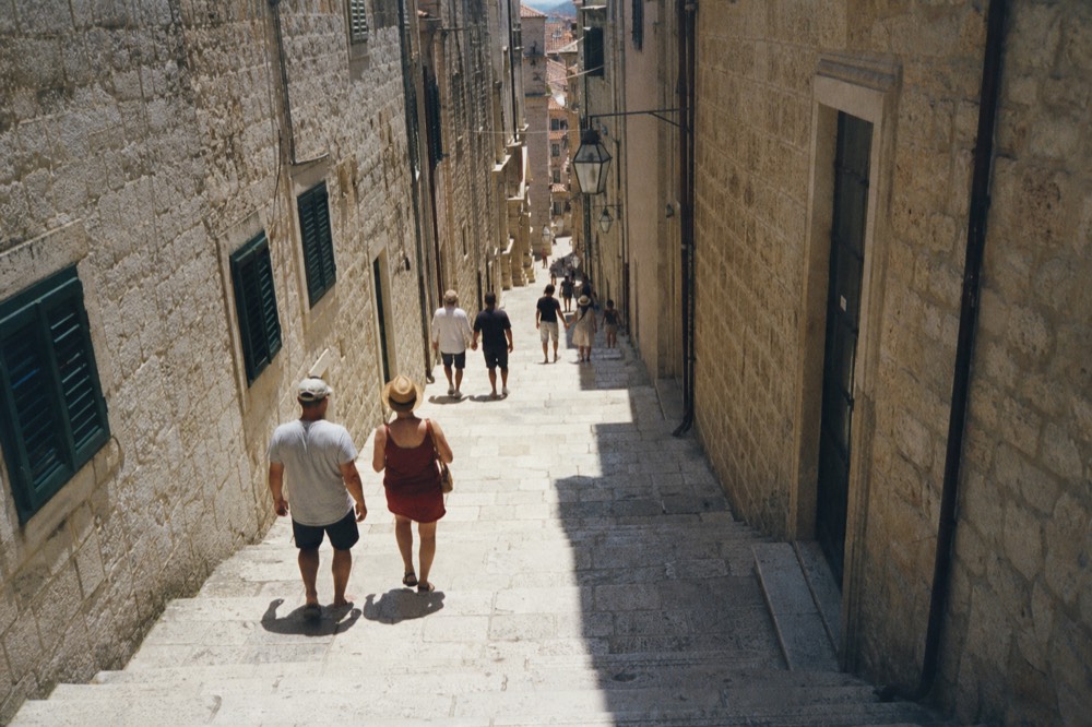 A narrow street in Dubrovnik's Old Town with stone buildings and no cars, only pedestrians walking