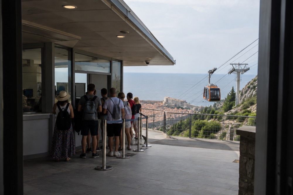 The cable car ticket office at the lower station with a short queue of tourists under a shaded awning