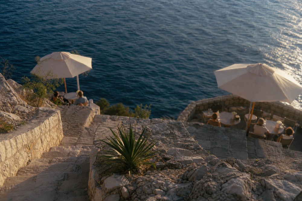 A simple cliffside bar terrace with tables and umbrellas above the open sea