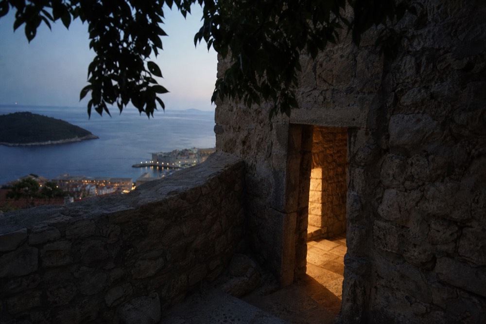 A low doorway in a rough stone wall at golden hour, warm light on the worn threshold