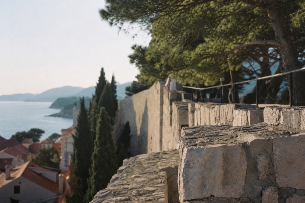 Ancient stone city walls above red rooftops and the sea