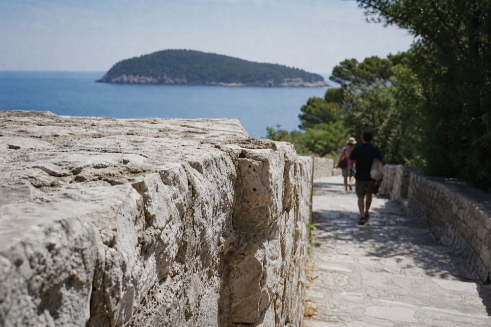Walkers on the walled path above the sea with Lokrum island in the distance
